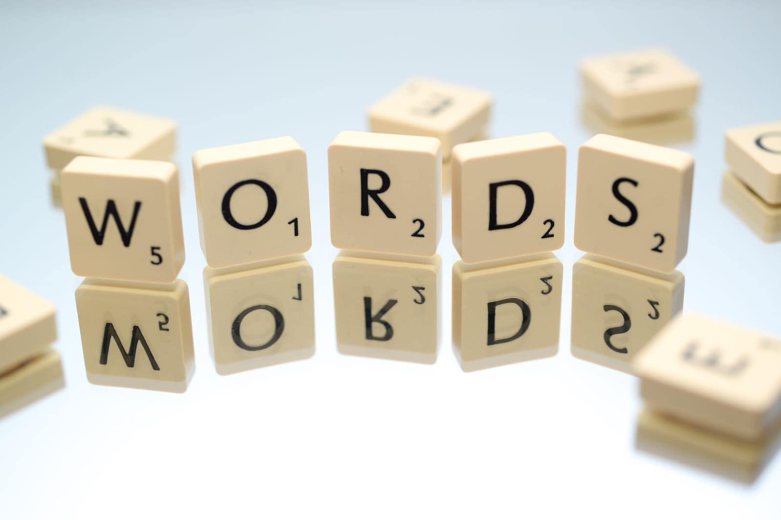 Scrabble tiles spelling the word WORDS, reflected on a glass table. Photo via Pexels (photo 695571).