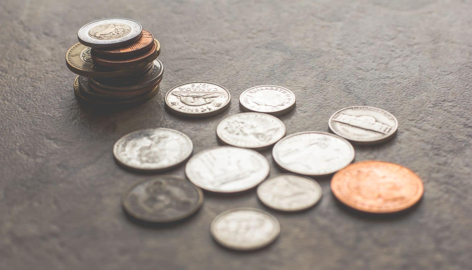 Loose coins scattered across a slate bench. Photo via Pexels (photo 1006060).