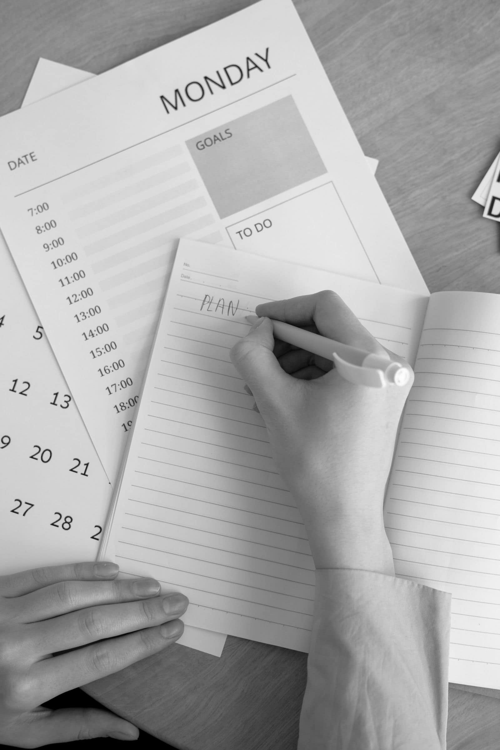 A hand writing a plan in a notebook. Photo by Hanna Pad via Pexels.