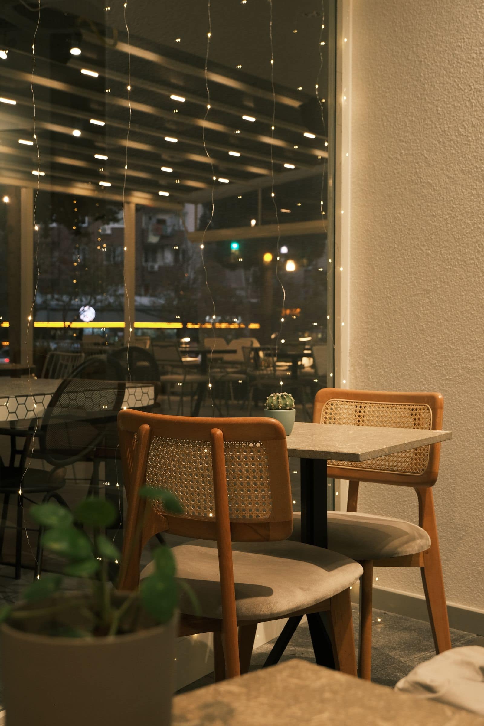 Empty cafe tables and chairs under fairy lights at dusk. Photo by Pexels via Pexels.