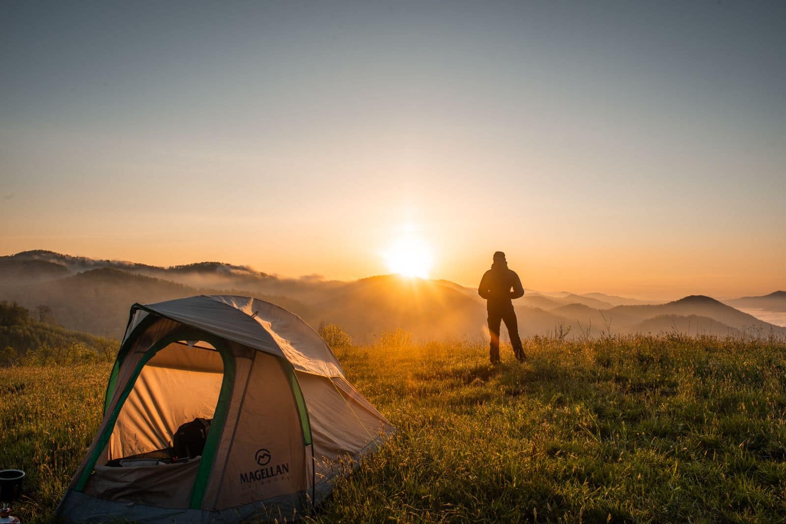 A camper beside a tent at dusk. Photo by (Pexels) via Pexels.