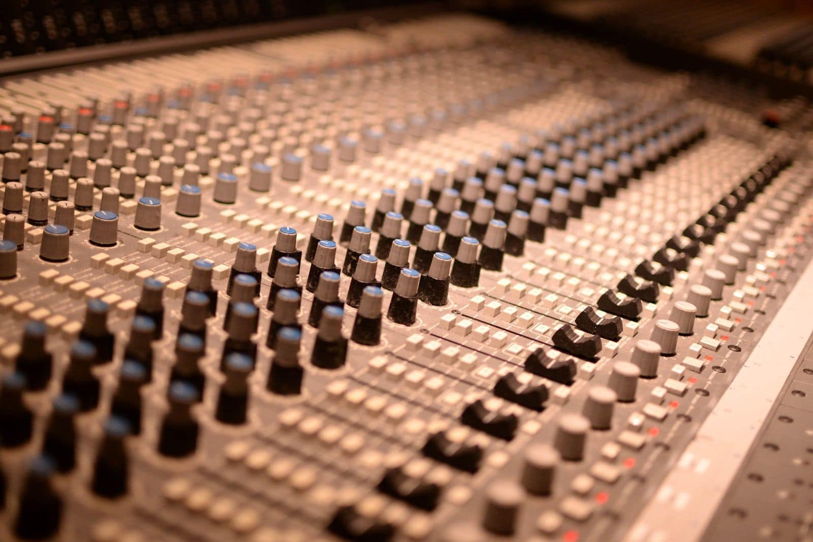 A large studio mixing console with rows of knobs and faders stretching into the distance. Photo by Pixabay via Pexels.